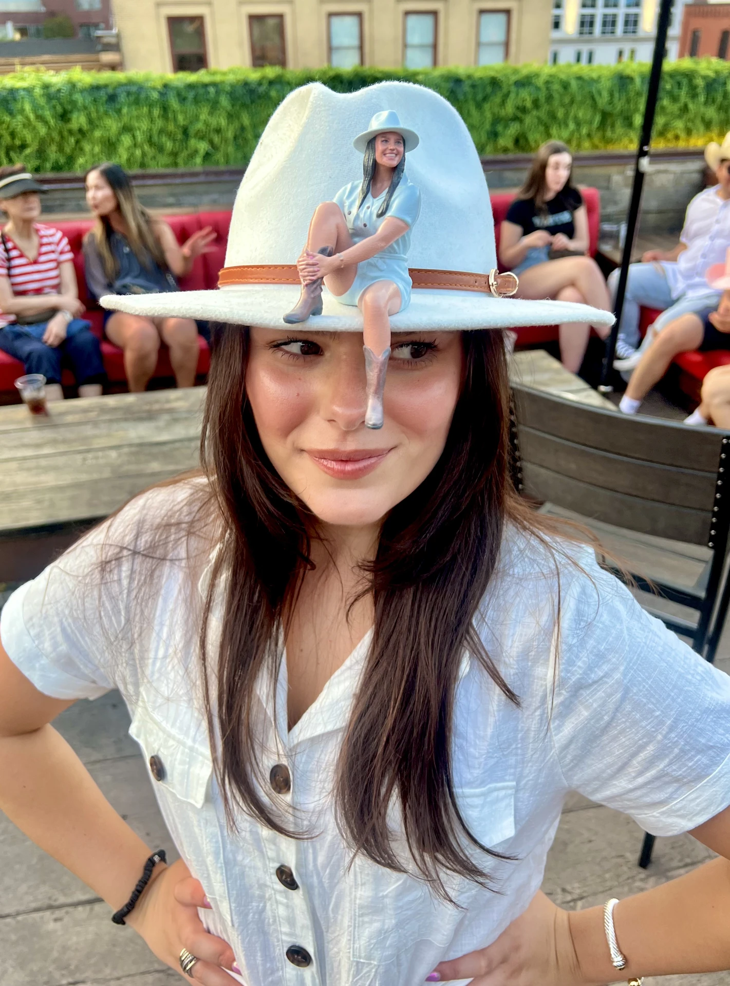 Miniature 3D-printed replica of a woman in a cowgirl hat, perched on the hat brim of the real person who was scanned